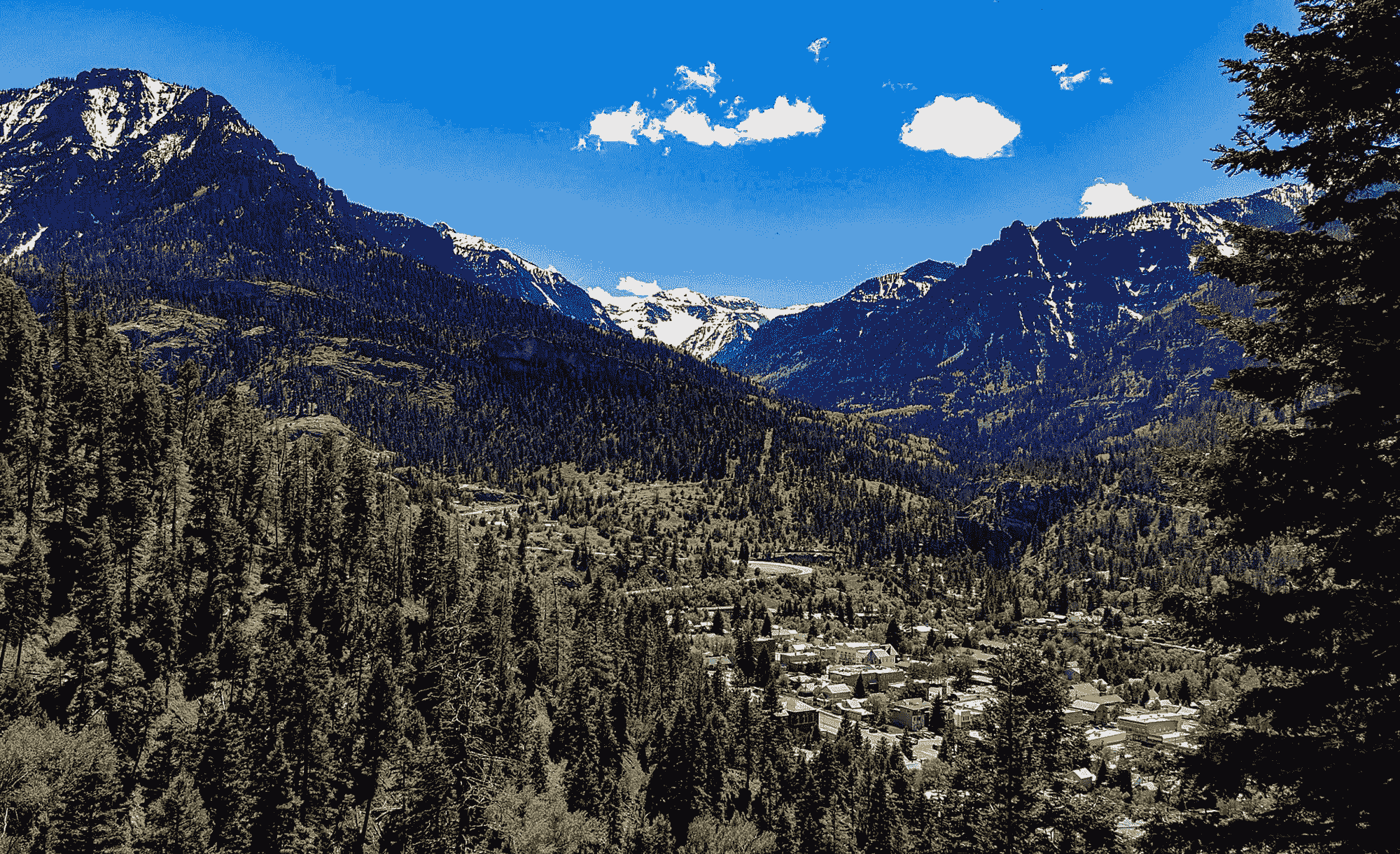 Mountain valley town surrounded by pine forests and snow-capped peaks.