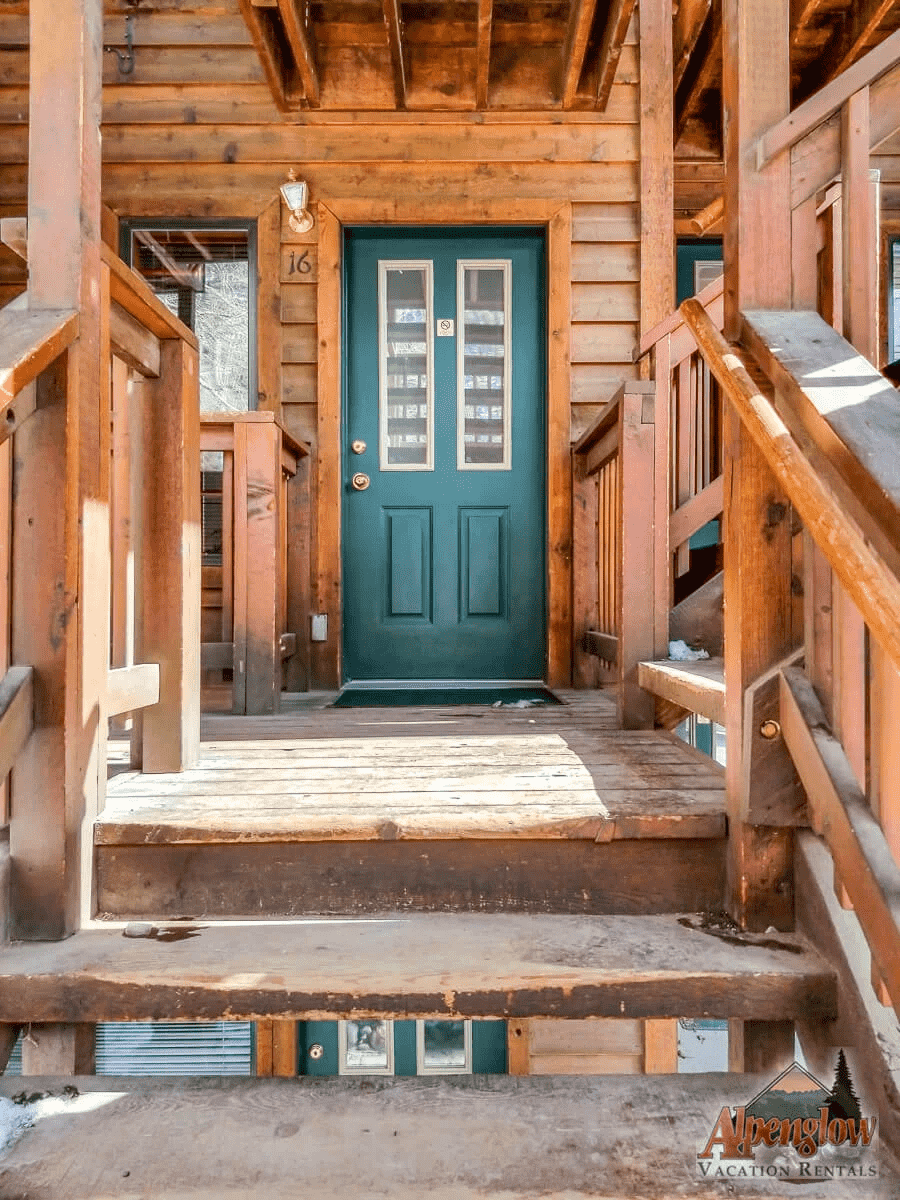 Wooden cabin entrance with green door and stairs.