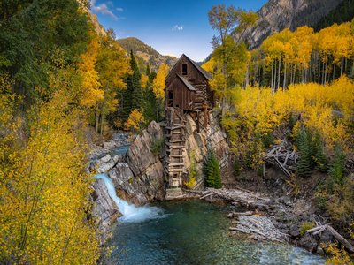 Wooden cabin on rocky cliff above clear waterfall in autumn forest