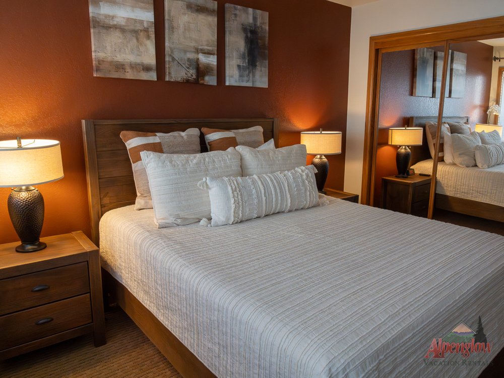 A neatly made bed with neutral bedding, two nightstands with lamps, abstract art above the headboard, and a mirrored closet in a cozy bedroom.