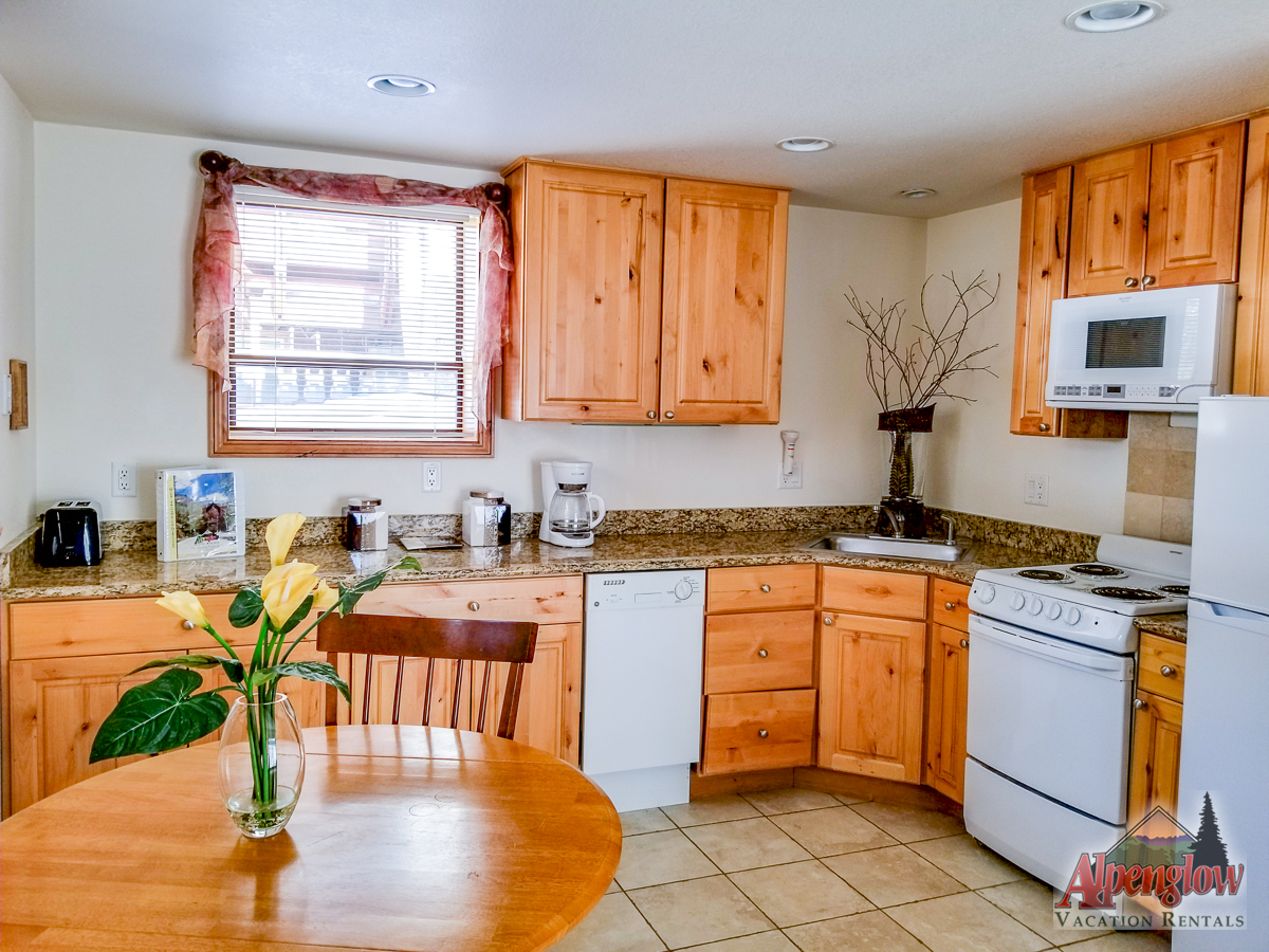A kitchen with wooden cabinets, white appliances, granite countertops, and a round dining table with a yellow flower arrangement.