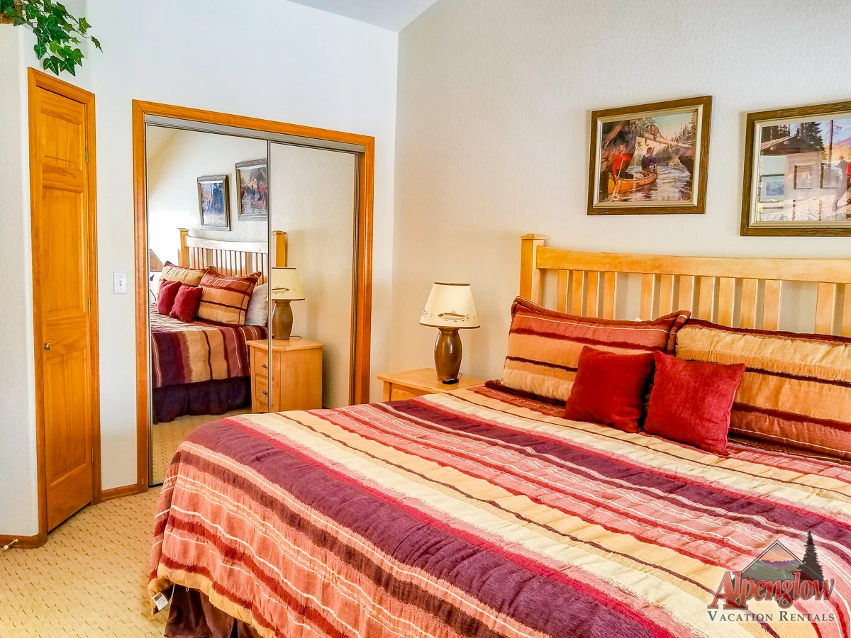 A bedroom in one of our vacation home rentals features a large wooden bed covered in a multicolored striped comforter, two bedside lamps, a mirrored closet door, and two framed paintings on the wall.